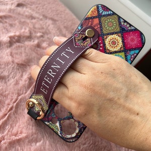 May include: A colorful phone case with a geometric pattern and a brown strap with the word "ETERNITY" printed on it.