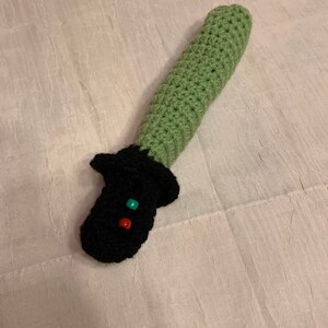 Puede incluir: Un juguete de sable de luz de crochet verde y negro con cuentas rojas y verdes.