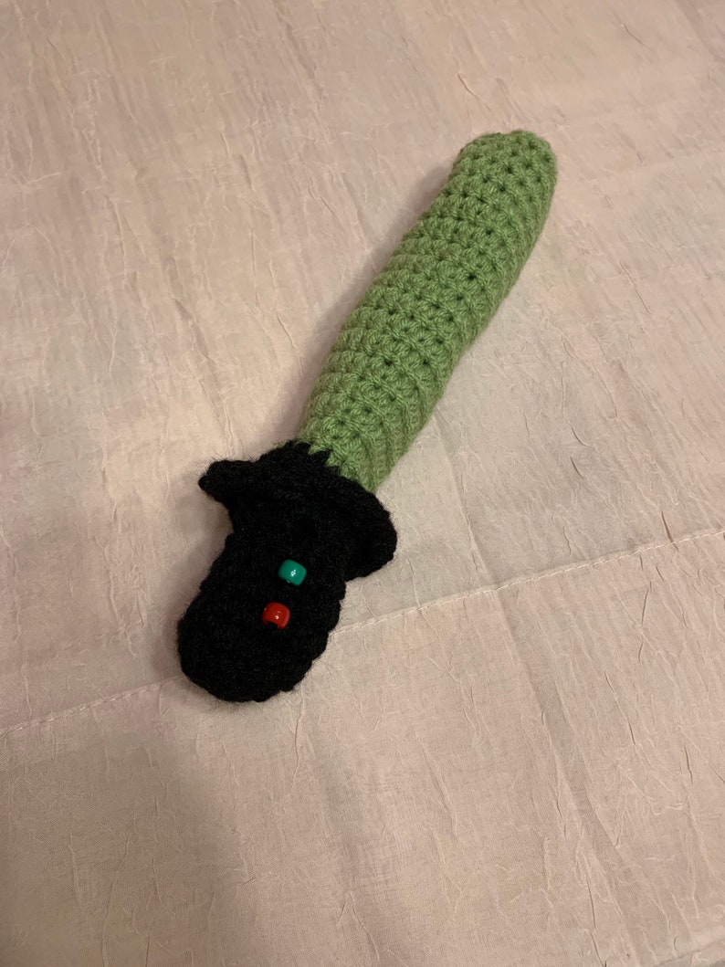Puede incluir: Un juguete de sable de luz de crochet verde y negro con cuentas rojas y verdes.