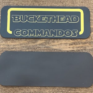 May include: Black rectangular sticker with yellow text that reads "Buckethead Commandos".