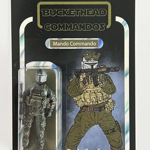 Pode incluir: Figura de ação colecionável de um Mando Commando, embalada em um cartão preto com o texto "BUCKETHEAD COMMANDOS". A figura está em uma caixa de plástico transparente. O cartão também apresenta uma ilustração do personagem. Maiores de 18 anos Colecionável.