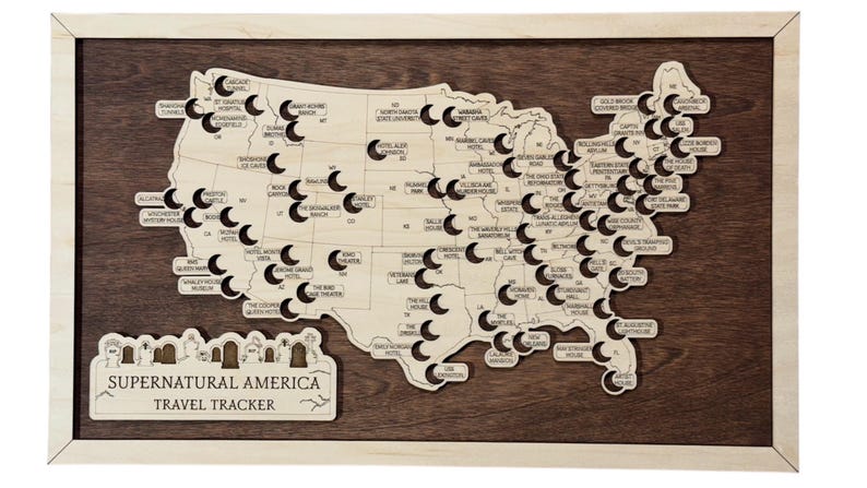 May include: A wooden map of the USA, featuring cut-out locations and labels, set against a dark brown backdrop and framed in light wood. The text "Supernatural America Travel Tracker" is displayed at the bottom of the map.