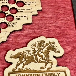 K&ouml;nnte beinhalten: Holz-Pferderennkarte mit einem Ausschnitt eines Pferdes und Jockeys sowie einer Karte des Nordostens der Vereinigten Staaten. Der Text "JOHNSON FAMILY HORSE TRACK BUCKET LIST MAP" wird unten angezeigt.