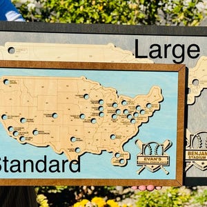 May include: Wooden map of the United States with baseball stadium locations. The map is framed in wood and has a light blue background. The text "Standard" and "Large" are visible. The map includes the text "Evan's Baseball Stadium Visits" and "Benjamin's Stadium Tour".