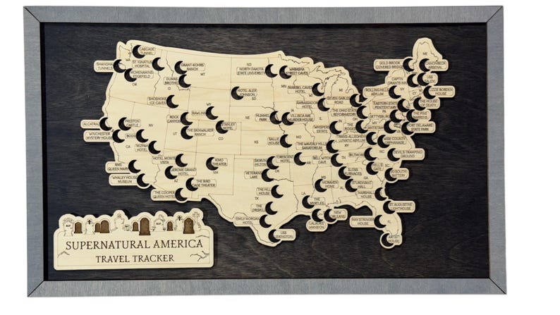 May include: Wooden map of the United States in a grey frame, with cut-out shapes and labels marking locations. The map includes the text "Supernatural America Travel Tracker" at the bottom.