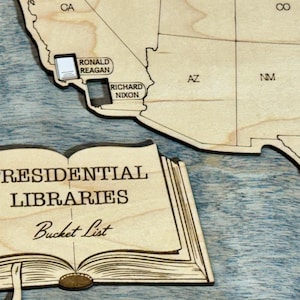 May include: Wooden map of the United States with laser-cut state outlines and names. Includes a separate wooden book-shaped piece with the text "PRESIDENTIAL LIBRARIES Bucket List". The map has pins for Ronald Reagan, Richard Nixon, Dwight D. Eisenhower, and Lyndon Baines Johnson.