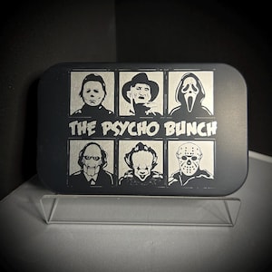 May include: A black metal box with a silver engraved image of six horror movie characters. The characters are Michael Myers, Freddy Krueger, Ghostface, Pinhead, Pennywise, and Jason Voorhees. The text "THE PSYCHO BUNCH" is engraved below the characters.