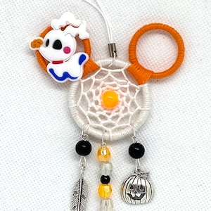 Könnte beinhalten: Weißer und orangefarbener Traumfänger zum Thema Halloween mit einem Geistercharakter-Anhänger, schwarzen und orangefarbenen Perlen, einer silbernen Feder und einem silbernen Kürbis-Anhänger.