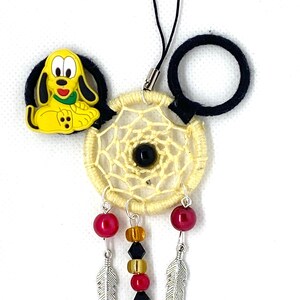 Könnte beinhalten: Ein gelber und schwarzer Traumfänger mit einem Pluto-Charakter-Anhänger, schwarzen Perlen und silbernen Federn. Der Traumfänger ist an einem schwarzen Handy-Anhängerband befestigt.