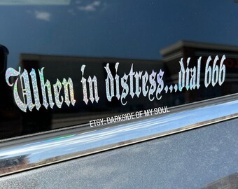 May include: A silver glitter decal on a black car window that reads "When in distress...dial 666" with the text "Etsy-Darkside of my soul" below.