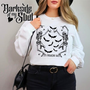 May include: White sweatshirt with a graphic of two skeletons dancing with bats and the text "It's Freaking Bats".