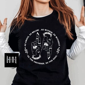 May include: Black t-shirt with a white graphic design featuring two hands with symbolic markings. The text reads "As above, so below. As within, so without. As the universe, so the soul."