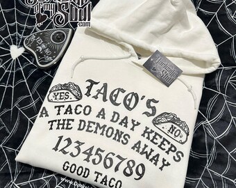 May include: White hooded sweatshirt with a black graphic print of a Ouija board with the text "Taco's A Taco A Day Keeps The Demons Away 123456789 Good Taco" and the website address "www.DarksideOfMySoul.com".