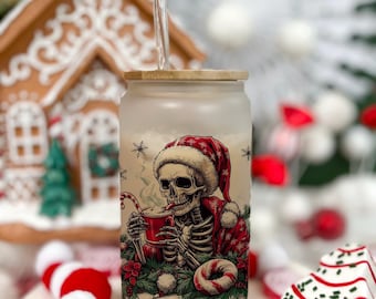 May include: Frosted glass tumbler with a bamboo lid. The tumbler features a skeleton wearing a Santa hat and coat, drinking from a red mug with a candy cane. The design includes snowflakes and the word "YOMSE".