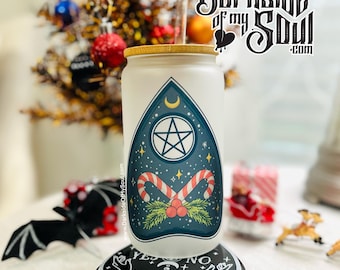 May include: White tumbler with a blue and green design featuring a pentagram, crescent moon, and candy canes. The tumbler has a gold lid and a black base with a Ouija board design.