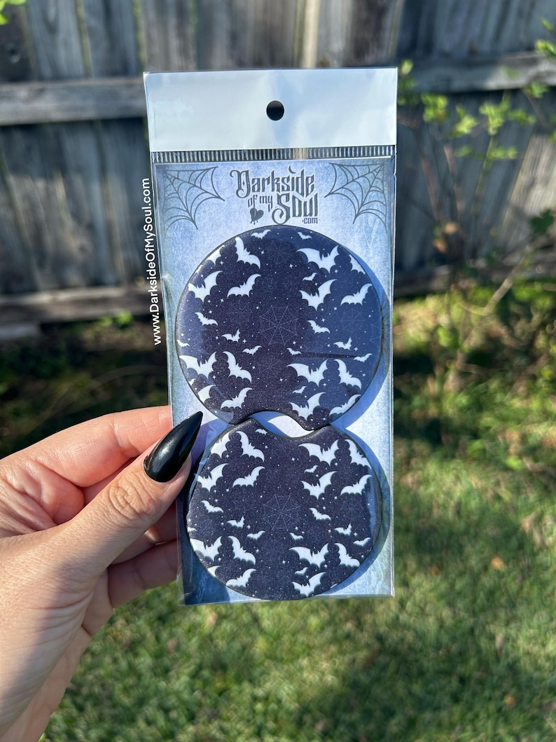 May include: Two black and white round coasters with a pattern of white bats on a black background. The coasters are packaged in a clear plastic bag with a white header card that says "Darkside of my Soul.com".