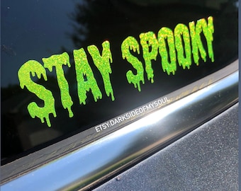 May include: Green glitter vinyl decal with the text "STAY SPOOKY" in dripping letters. The decal is on a black car window.