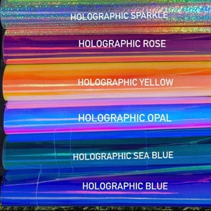 May include: A stack of six rolls of holographic vinyl in various colors, including sparkle, rose, yellow, opal, sea blue, and blue. Each roll has a label with the color name and the word "Holographic".