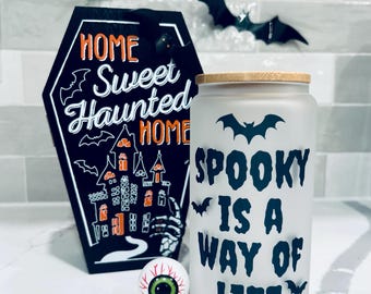 May include: Halloween-themed decor featuring a black coffin-shaped sign with "Home Sweet Haunted Home" text, a frosted glass tumbler with "Spooky is a Way of Life" text, and a decorative eyeball. Black bat cutouts are in the background.