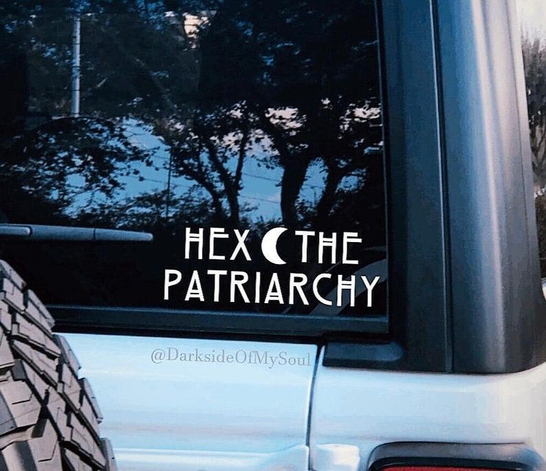 May include: White vinyl sticker on a black car window that says "Hex the Patriarchy" with a crescent moon symbol. The sticker also includes the text "@DarksideOfMySoul".
