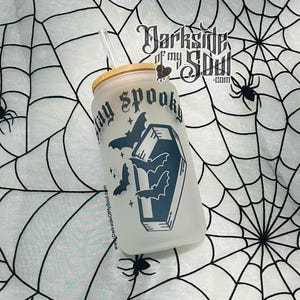 Puede incluir: Un vaso de vidrio esmerilado con un dise&ntilde;o en blanco y negro de un ata&uacute;d con murci&eacute;lagos volando a su alrededor. El texto "Stay Spooky" est&aacute; impreso en el vaso. El vaso tiene una tapa de bamb&uacute; y una pajita.