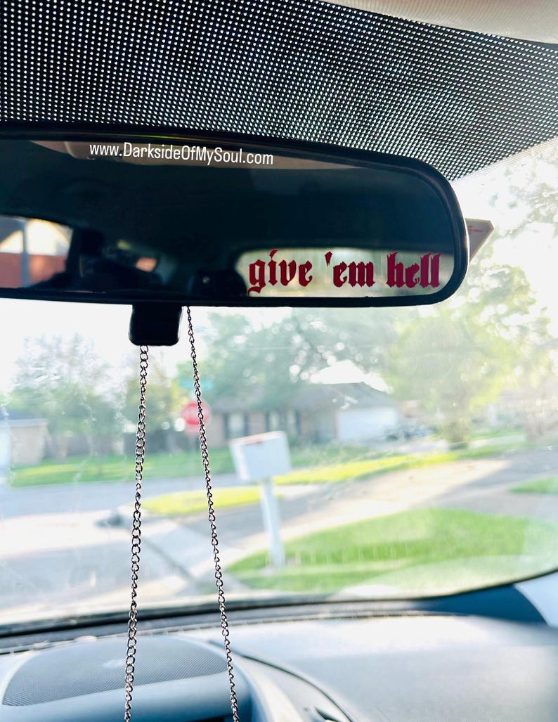 May include: A rearview mirror with a red "give 'em hell" sticker attached to it. The mirror is hanging from a silver chain.