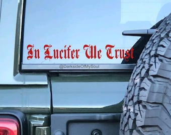 May include: A green car with a red sticker on the back window that says "In Lucifer We Trust" with the social media handle "@DarksideOfMySoul" underneath.