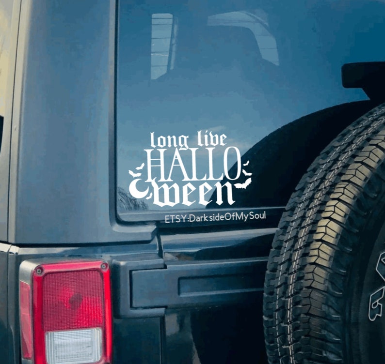 May include: A white vinyl decal with the text "long live HALLOWEEN" in a gothic font with bats on either side. The decal is on the back window of a black Jeep. The text "ETSY-DarksideOfMySoul" is below the decal.