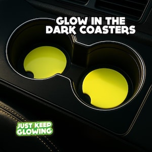 May include: Two bright yellow glow-in-the-dark coasters inside a car's cup holders. The coasters have a small notch for easy removal. The text "GLOW IN THE DARK COASTERS" is above the cup holders. The phrase "JUST KEEP GLOWING" is in the lower left corner.