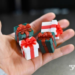 May include: Four miniature gift boxes in hand, each with a bow. Two are white with red ribbons, and two are green with red ribbons. The gifts are small, perfect for a holiday or special occasion.