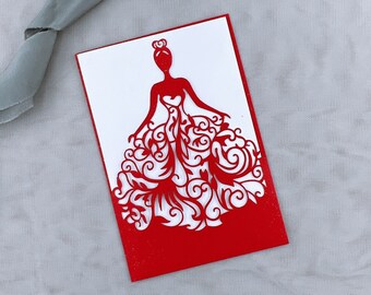 May include: Red laser cut invitation card with a white silhouette of a woman in a gown with a heart on her chest. The gown is decorated with intricate floral designs.