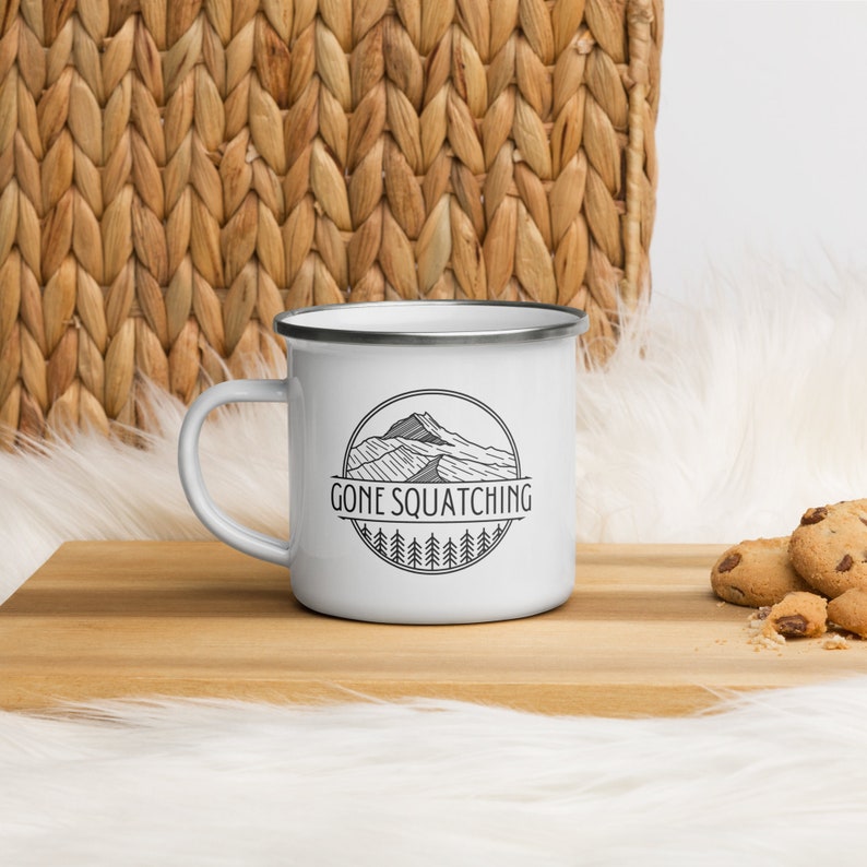 May include: White enamel camping mug with a black and white graphic of a mountain range and the text "Gone Squatching".