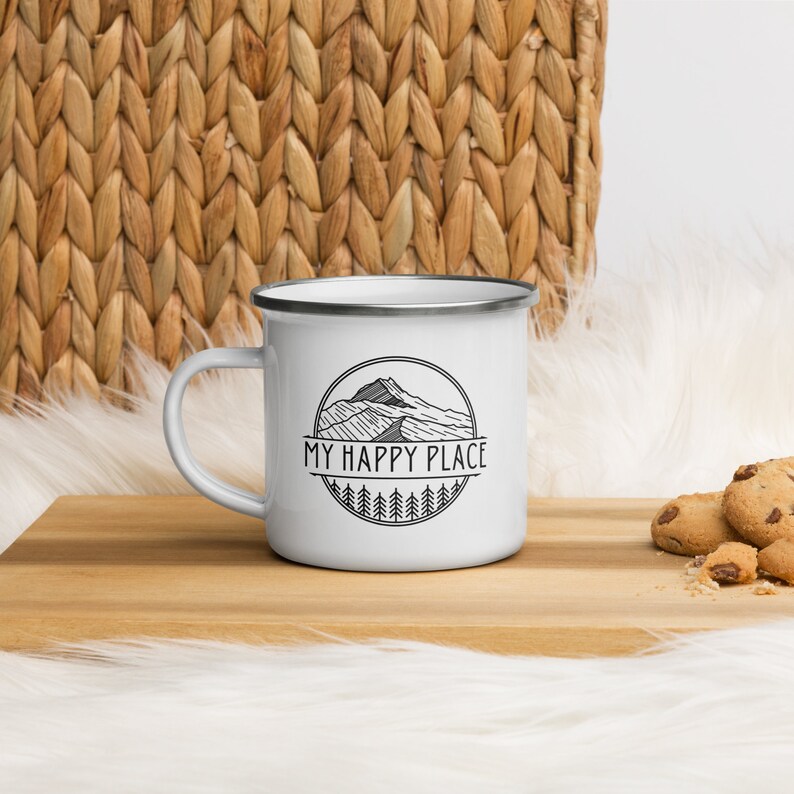 May include: White enamel camping mug with a black and white graphic of a mountain range and the text "MY HAPPY PLACE".