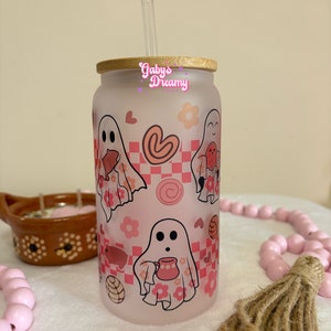 May include: A frosted glass tumbler with a bamboo lid and a straw. The tumbler features a pink and white design with ghosts, hearts, and flowers. The text "Gaby's Dreamy" is printed on the tumbler.