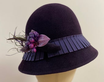 Deep eggplant purple velour fur felt cloche hat with pleated trim around crown, fancy trim and feathers. 22 1/2” hd sz only one.