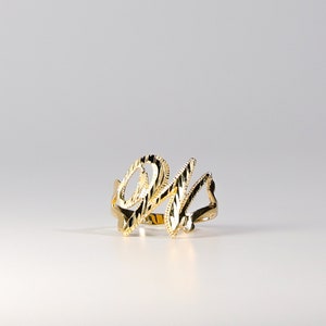 Puede incluir: Un anillo dorado con las letras "OM" en escritura cursiva. El anillo tiene una superficie texturizada y está sobre un fondo blanco. Es una pieza de joyería.
