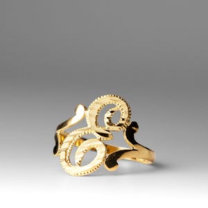 Puede incluir: Un anillo de oro con un diseño delicado y adornado con la letra "G".