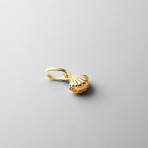 May include: A gold-tone seashell charm with a pearl inside. The charm has a loop for attaching to a necklace or bracelet.