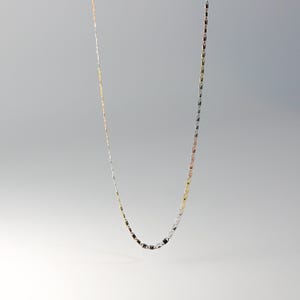 May include: A delicate gold, silver, and rose gold chain necklace. The chain is made of small, linked oval shapes.