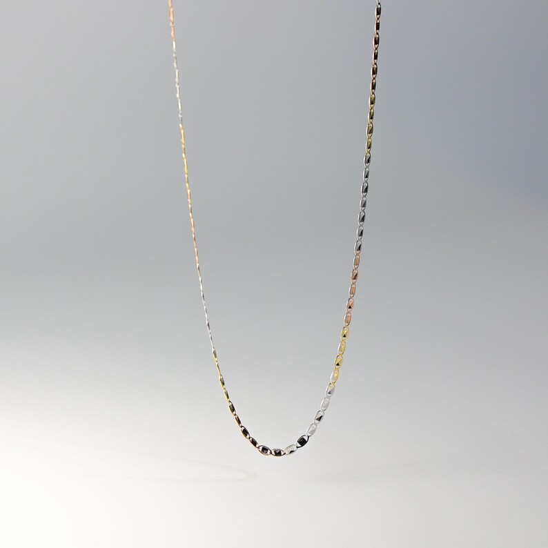 May include: A delicate gold, silver, and rose gold chain necklace. The chain is made of small, linked oval shapes.