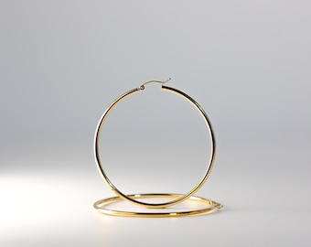 Puede incluir: Un par de pendientes de aro de oro. Los pendientes son grandes y de forma circular.