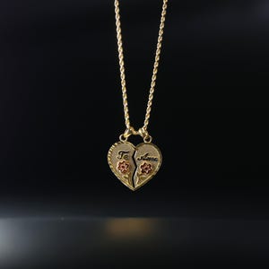 May include: A gold chain necklace with a broken heart pendant. The pendant is made of two pieces, each with a half of the heart. One half says "Te" and the other half says "Amo". There are two red flowers on the pendant.