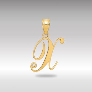 Può includere: Un ciondolo color oro a forma di lettera "X" in corsivo. Un piccolo diamante rotondo è incastonato vicino alla parte inferiore della lettera. Il ciondolo ha un anello nella parte superiore per una catena.