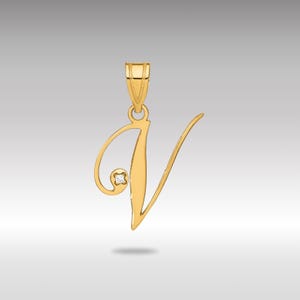 Könnte beinhalten: Ein goldfarbener Anhänger in Form des Buchstabens "V". Der Anhänger hat einen kleinen, runden Diamantakzent. Das Design ist eine Schreibschrift mit einer Schlaufe oben und einer gebogenen Linie, die sich nach unten erstreckt. Der Anhänger ist an einer passenden goldenen Öse aufgehängt.