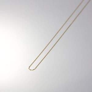 May include: A gold chain necklace with a delicate, thin design. The chain is made of a smooth, shiny metal and has a simple, elegant style.