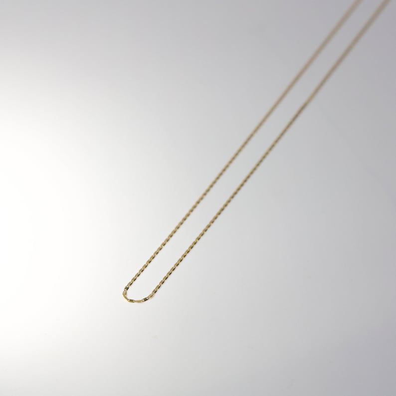 May include: A gold chain necklace with a delicate, thin design. The chain is made of a smooth, shiny metal and has a simple, elegant style.