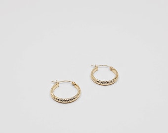 May include: Two gold-colored hoop earrings with a textured, diamond-like pattern. The earrings are small and circular, with a simple clasp closure. The jewelry is set against a plain white background.