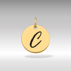 Puede incluir: Colgante redondo dorado con la letra "C" cursiva negra en el centro. El colgante tiene un pequeño lazo en la parte superior para una cadena. El fondo es un degradado de gris claro y dorado.