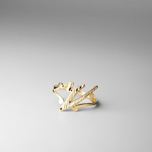 Puede incluir: Un anillo de oro con un diseño estilizado de la letra 'Z'. El anillo está hecho de metal texturizado y tiene un aspecto simple y elegante.