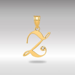 May include: A gold-coloured pendant in the shape of the letter "Z". The pendant features a small, sparkling gemstone embedded in the design. The letter is in a cursive font, with a loop at the top for a chain.